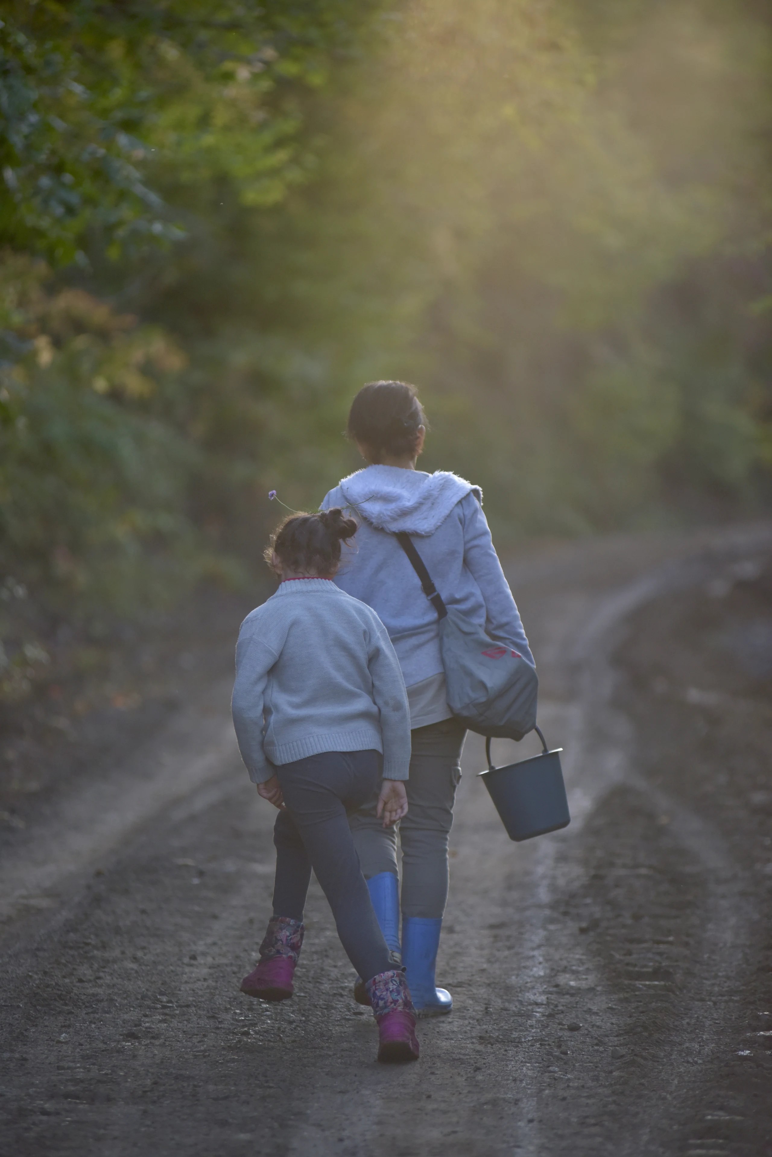 Two figures walking along a forest road with a bucket.