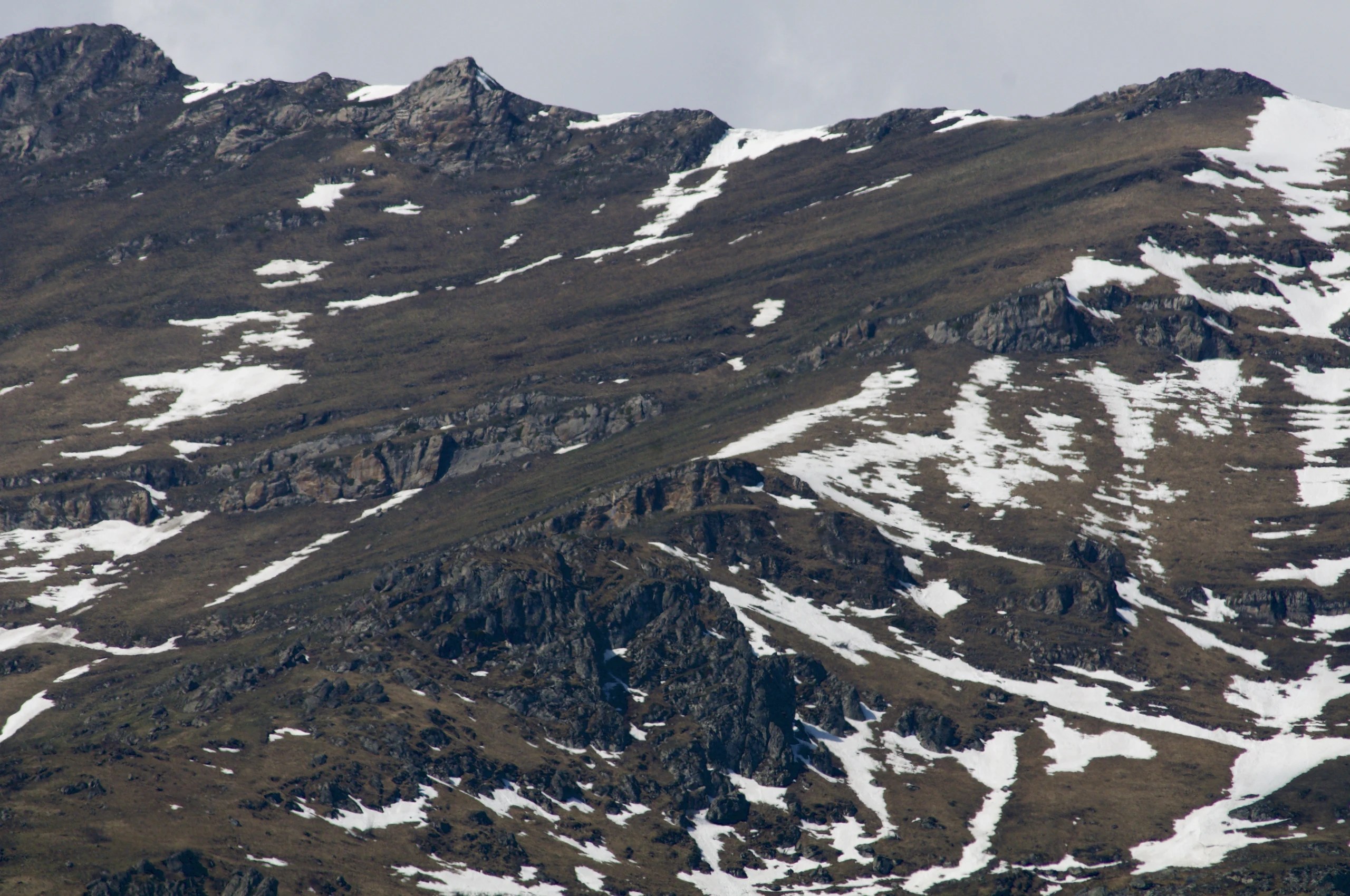 Snow patches on dark mountain slopes beneath a rocky ridge.