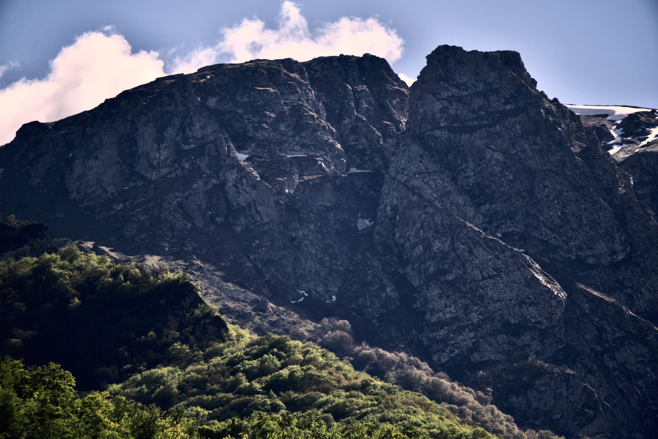 Dark cliffs and a green forest slope beneath patches of snow.