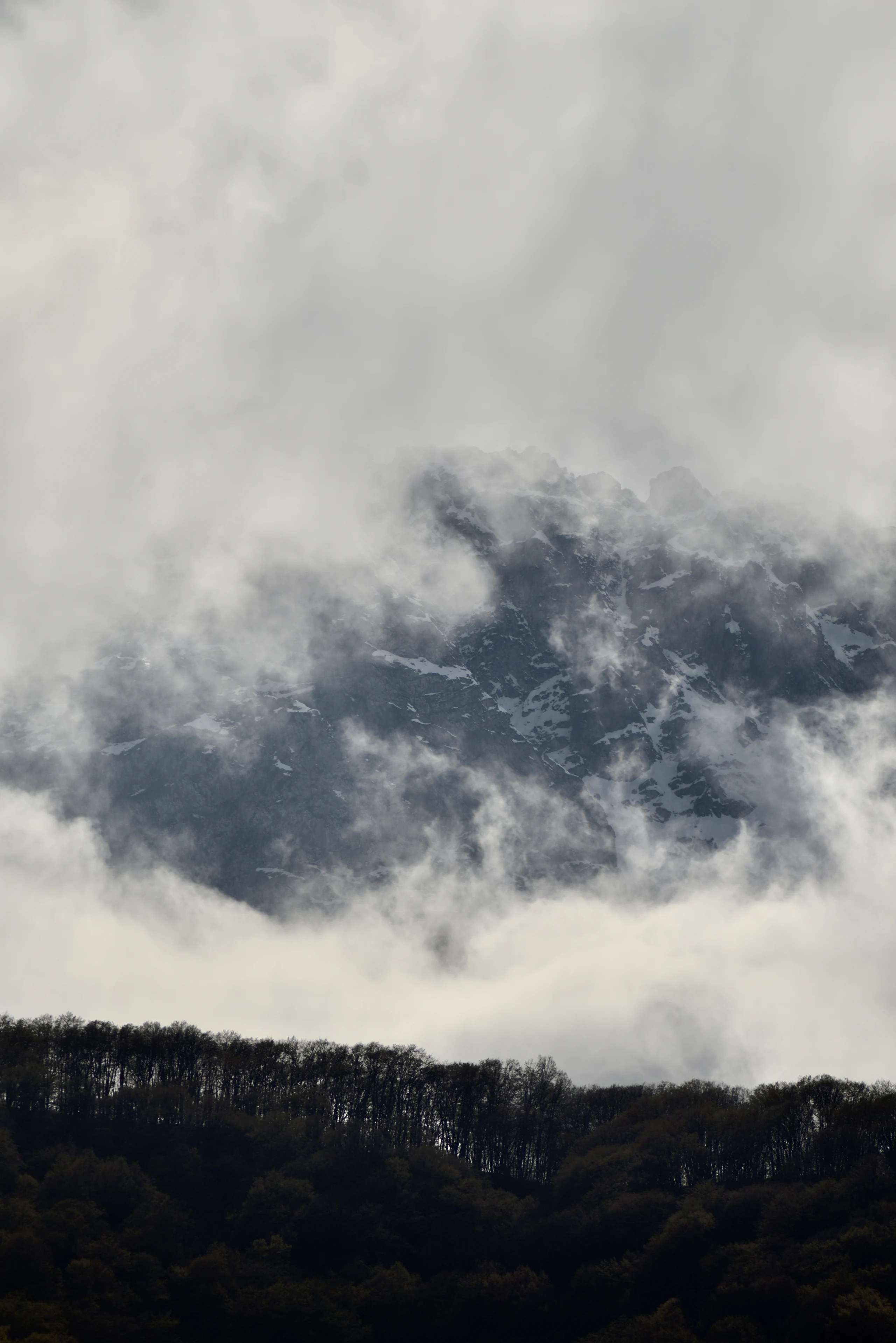 A snow-marked mountain face partly hidden by low clouds.