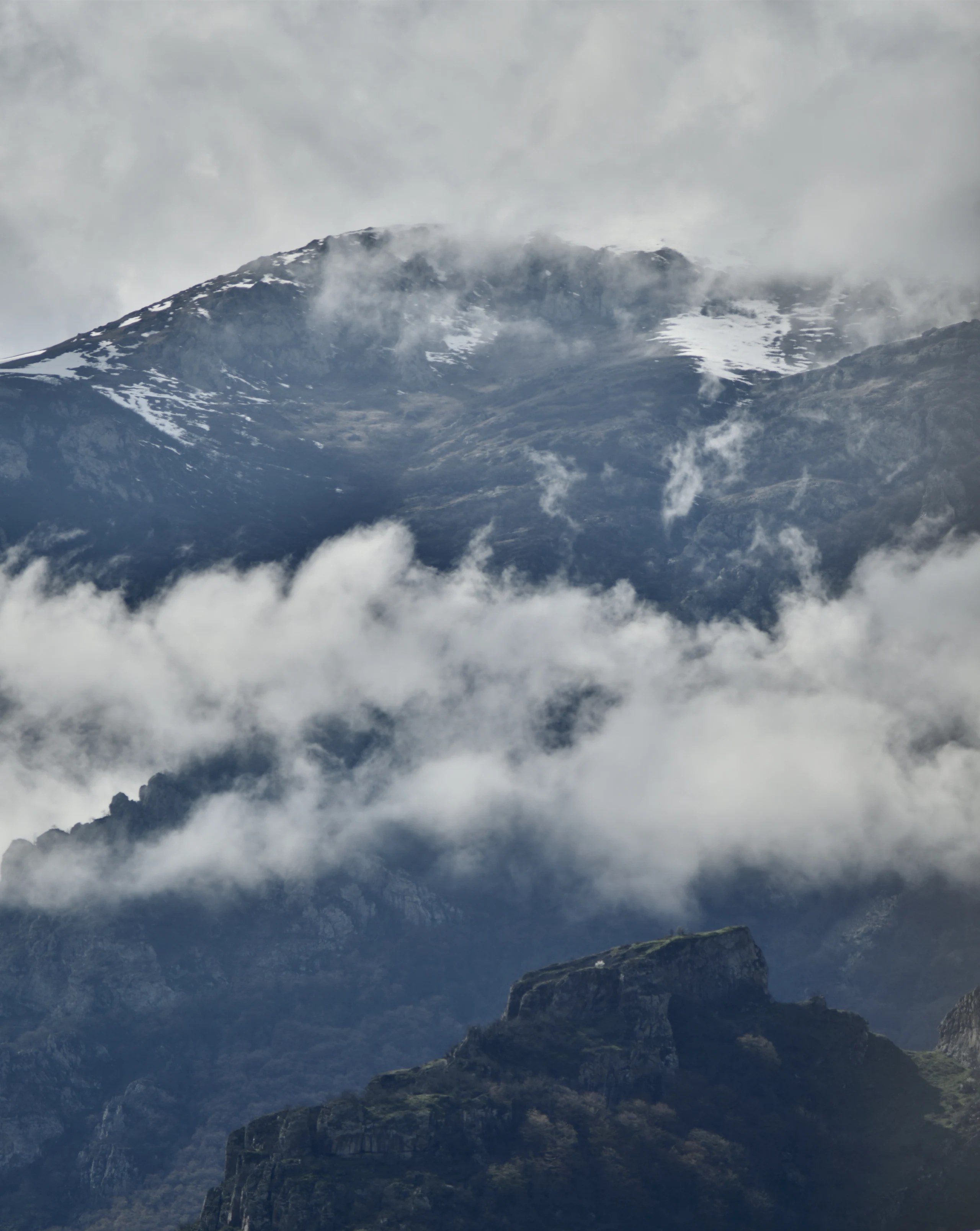 Low clouds around a broad mountain face and dark cliffs.