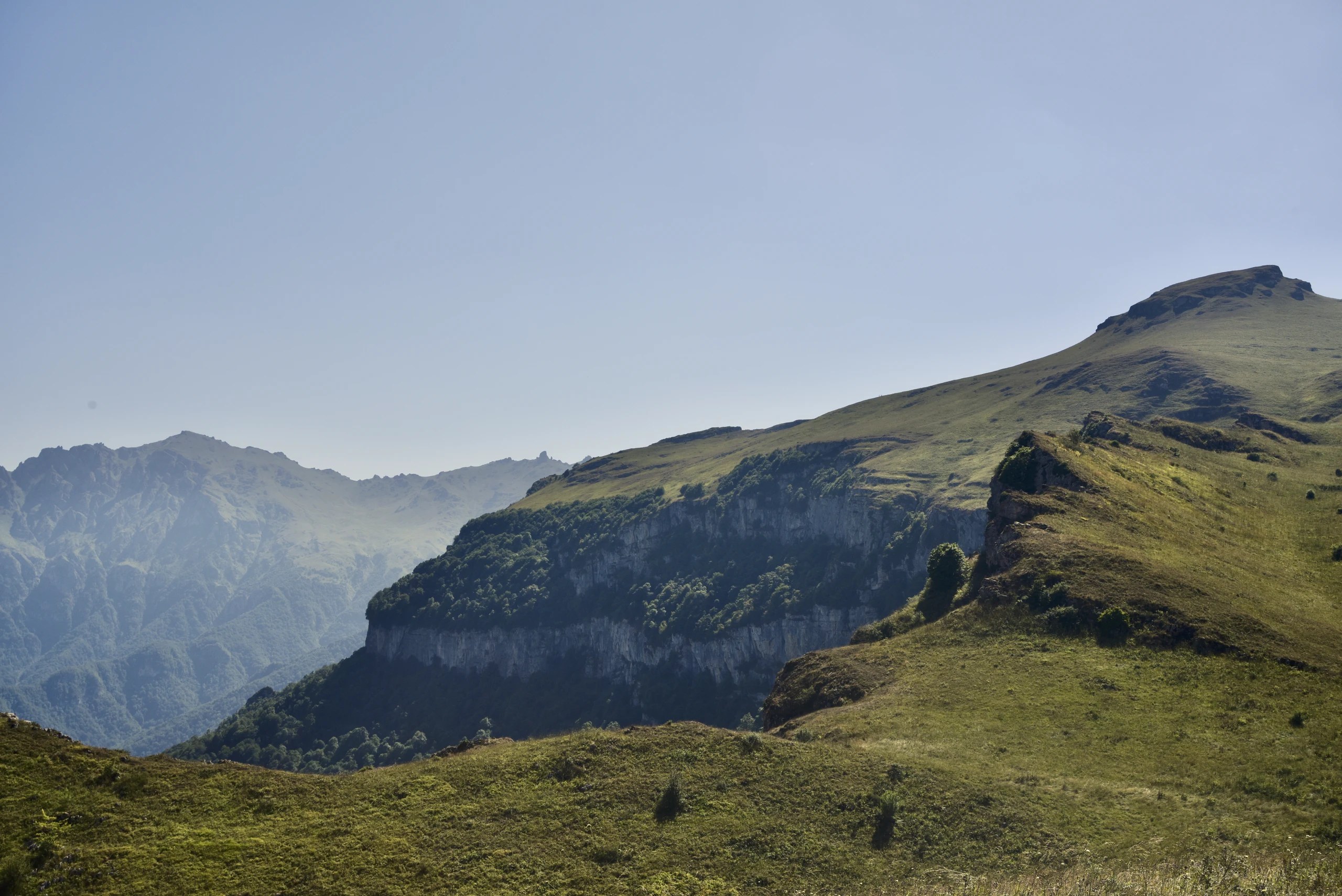 Grassy mountain slopes above pale cliffs under a clear sky.