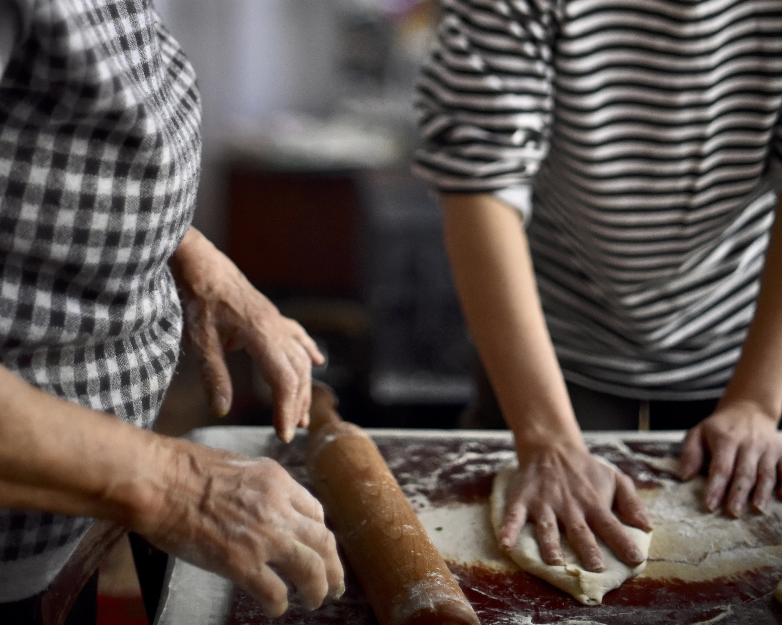 Two people rolling and shaping dough on a floured worktable.
